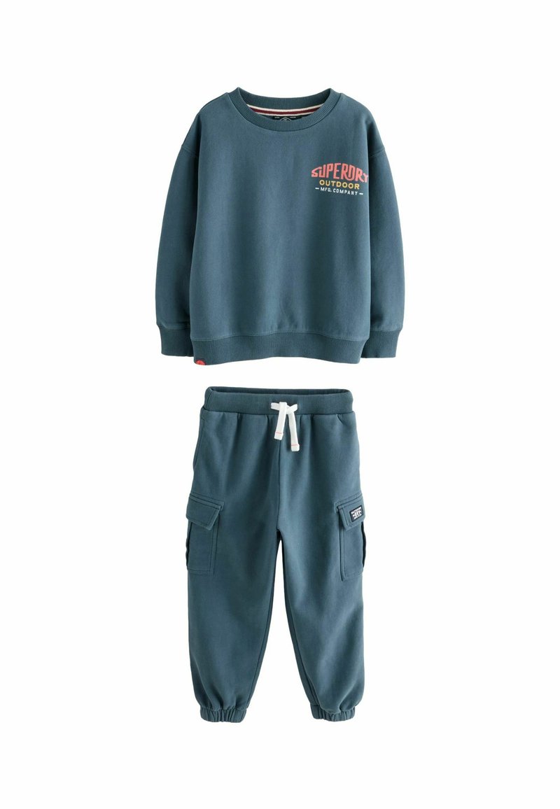 Felpa blu per bambini con la scritta "Superdry Outdoor" abbinata a pantaloni jogger in stile cargo con stringa bianca.