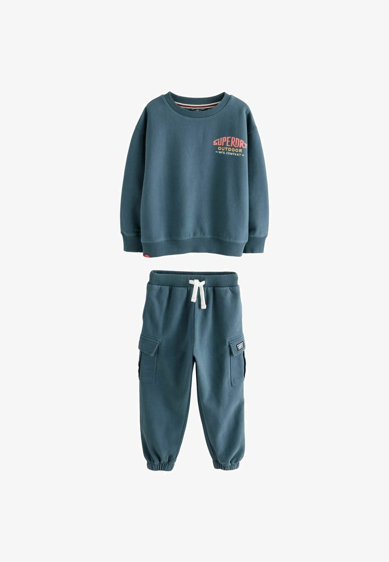 Blauer Kinder-Sweatshirt mit dem Schriftzug "Superdry Outdoor", kombiniert mit passenden Jogginghosen im Cargo-Stil mit weißer Kordel.