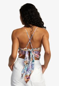 Colorful floral-patterned crop top with a tie-back design, white fabric waist, and thin adjustable straps crossing at the back.