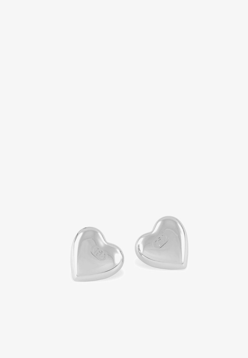 Paire de boucles d'oreilles clous en forme de cœur en argent poli avec un logo gravé subtil sur chaque, présentée sur un fond blanc.