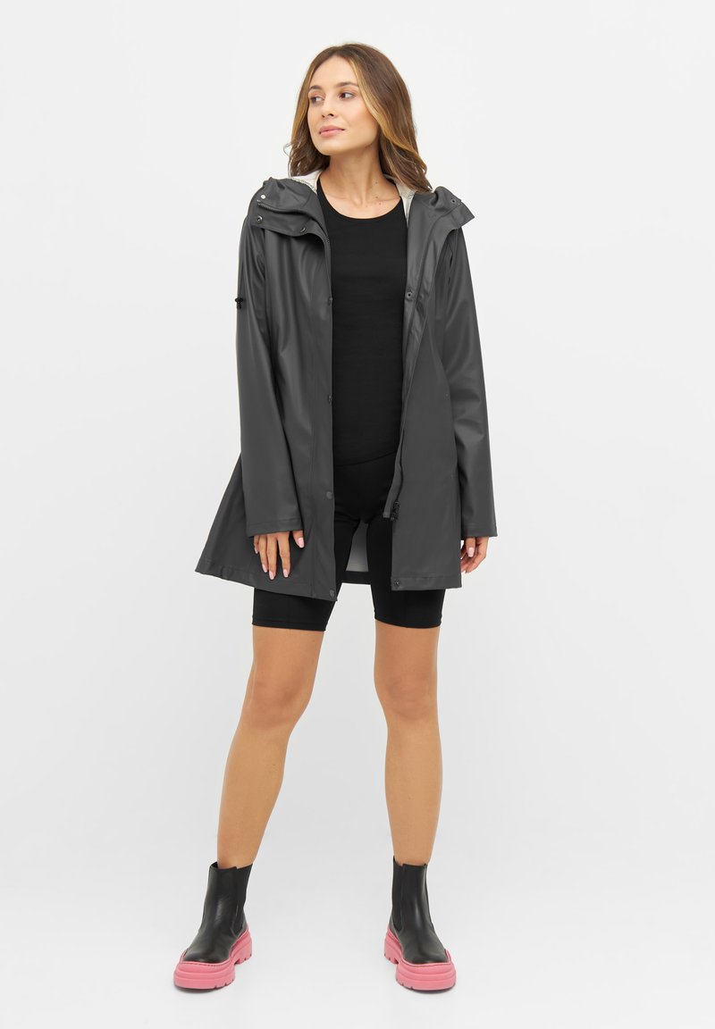 Waterdichte grijze regenjas met een capuchon; getailleerde stijl; zachte textuur;laag over een zwarte top en zwarte shorts; gecombineerd met zwart en roze laarzen.