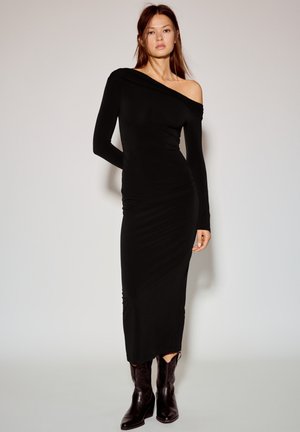 Fekete, testhez simuló ruha hosszú ujjakkal és vállat szabadon hagyó kialakítással. Sima anyagból; oldalsó ráncolással és középhosszúsággal, a lábszár közepéig ér.