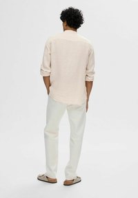 Camisa de botones rosa claro con mangas arremangadas, combinada con pantalones blancos y zapatos tipo slip-on beige. Diseño sencillo y relajado.