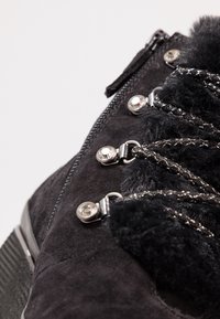 Stivale in suede nero con chiusura a zip, dettagli in pelliccia, hardware in tono argento e lacci decorativi. Presenta accenti testurizzati e una suola robusta.