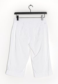 Weiße Caprihosen, die an einem schwarzen Kleiderbügel hängen, mit glattem Material, zwei Gesäßtaschen und aufgerollten Säumen.