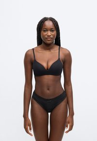 Μαύρο σουτιέν και ταιριαστά εσώρουχα με δαντέλα. Λείο ύφασμα με ρυθμιζόμενους ιμάντες, διαθέτει κλασικό τριγωνικό σχέδιο στα κύπελλα και λεπτή διακοσμητική κορδέλα.