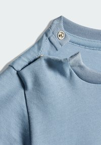 Svetlomodrá bavlnená tričkovina s rebrovaným dekoltom, obsahujúca patentky na pleciach a hladkú textúru po celom povrchu.