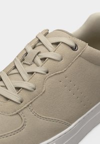 Baskets en daim beige avec bouts arrondis, lacets plats beiges, motif de perforations latérales et semelle en caoutchouc blanche.