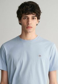 Světle modré tričko s krátkými rukávy vyrobené z měkké bavlny. Obsahuje malé logo na hrudi a klasický kulatý výstřih. Minimalistický design.