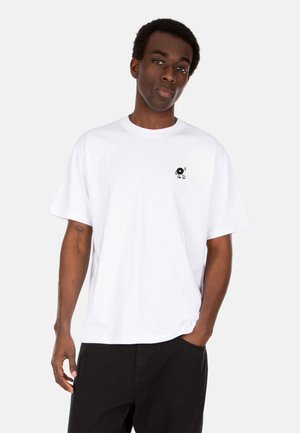 Weißes Baumwoll-T-Shirt mit kurzen Ärmeln und Rundhalsausschnitt, mit einem schwarzen Vinylgrafik auf der linken Brust. Kombiniert mit schwarzen Hosen.
