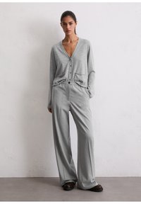 Cardigan grigio chiaro con scollo a V, chiusura con bottoni e tasche frontali abbinato a pantaloni a gamba larga grigio chiaro. Tessuto liscio, vestibilità comoda.