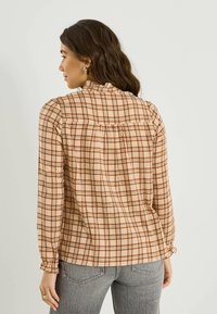 Chemise à manches longues à carreaux beige avec des motifs marron et rouille, dotée d'un col à volants, d'un dos froncé et de poignets élastiques.