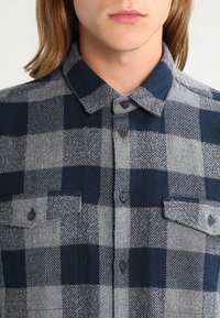 Geruite flanellen shirt in marineblauw en grijs. Beschikt over een kraag, knoopsluiting aan de voorkant en twee borstzakken met knoopsluiting. Zachte textuur.