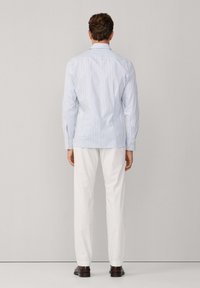 Herenlangsleefshirt in lichtblauw met witte verticale strepen, slim fit ontwerp, gebogen zoom, gecombineerd met witte broek en donkere schoenen.