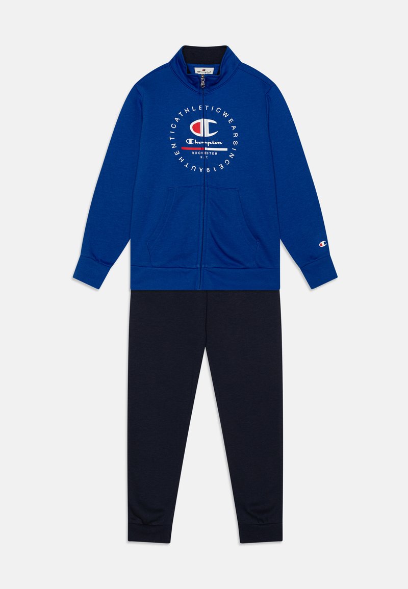 Chaqueta azul con cremallera y logo en la parte delantera, combinada con pantalones jogger azul marino. Ambos están hechos de una tela suave, con puños acanalados y bolsillos.