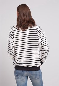 Bílo-černý pruhovaný svetr s dlouhými rukávy, žebrovanými manžetami a lemem, vyrobený z jemné tkaniny. Nosený s modrými džíny.