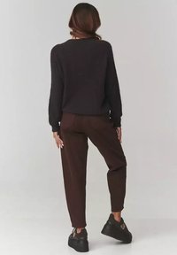 Ciemnobrązowy sweter z dzianiny z długimi rękawami, w połączeniu z brązowymi zwężającymi się spodniami i czarnymi sneakersami na platformie. Prosty, casualowy strój widziany z tyłu.