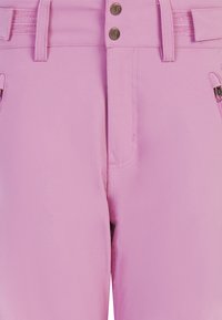 Close-up van pastelroze broeken met riemlussen, twee voorste ritszakken en dubbele metalen knopen bij de taille.