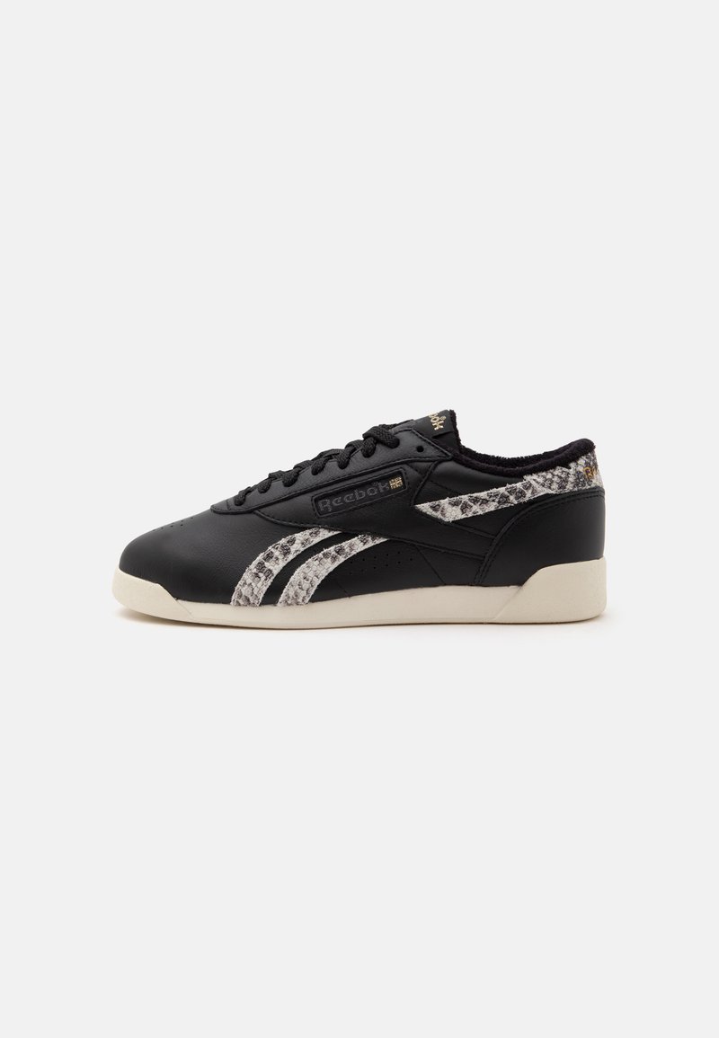 Μαύρο χαμηλό παπούτσι Reebok με λωρίδες φιδιού, μαύρα κορδόνια και μπεζ σόλα, εμφανιζόμενο από το πλάι σε λευκό φόντο.