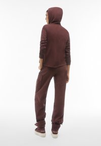 Set di felpa con cappuccio e pantaloni cargo abbinati di colore bordeaux. Tessuto morbido, design con cappuccio e polsini affusolati. I pantaloni della tuta sono dotati di tasche laterali e caviglie elasticizzate.