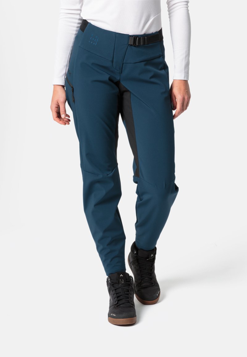 Teal buitenbroek met zwarte accenten, waterdichte stof, taps toelopende pasvorm en ritszakken. Draag het met zwarte wandelschoenen.