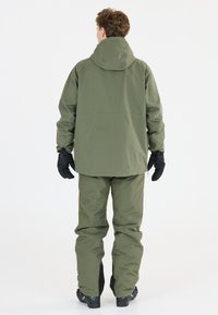 Vattentät grön skidjacka med huva, elastiska ärmar och matchande byxor. Handskar och stövlar synliga; skräddarsydd för utomhusaktiviteter.