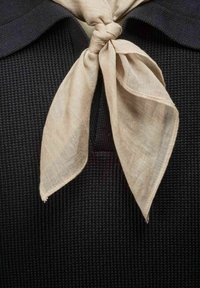 Sort tekstureret beklædning med krave, der har et lyst beige linnedscarf bundet i en knude foran.