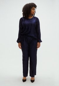 Tumesinise värvi kahest tükist koosnev volditud komplekt, mis koosneb pikakäistest särgist ja sobivatest püksidest, valmistatud kergekaalusest kangast, lõdva istuvusega ja sujuva tekstuuriga.