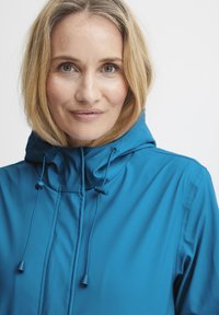 Blauwe lichtgewicht jas met een gestructureerde capuchon, verstelbare trekkoorden en een gladde textuur. Heeft een voorkant met rits en geen zichtbare patronen.