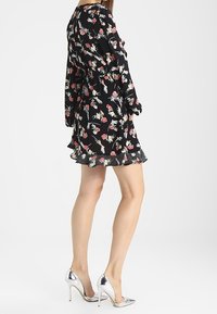 Černé květinové šaty s dlouhými rukávy, zdobené růžovými a bílými květy, s volánkovým lemem a puntíky, v kombinaci se stříbrnými vysokými podpatky.