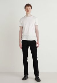 Îmbrăcăminte unisex formată dintr-un tricou alb simplu din bumbac și pantaloni negri slim-fit. Modelul poartă pantofi negri, stând pe un fundal neutru.