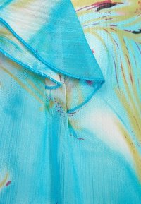 Tissu léger et transparent de couleur bleu vibrant avec un motif aquarelle en jaune et rose. Présente un col froncé avec des détails de couture délicats.