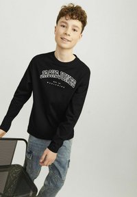 Fekete, hosszú ujjú pulóver fehér "JACK&JONES" logóval, kék farmer cargo nadrággal párosítva, amely folt zsebekkel és laza szabással rendelkezik.