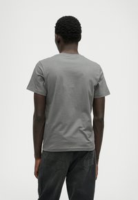 T-shirt cinza de algodão com mangas curtas, apresentando um decote redondo e uma textura suave, usada com jeans escuros.