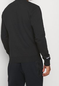 Svart sweatshirt i bomullsblandning, med rund hals, långa ärmar, ribbade muddar och en logotypdetalj på vänster ärm.