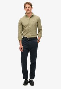 Licht olijfgroene button-up overhemd, donker marineblauwe broek, zwarte riem en zwarte schoenen. Slim fit, lange mouwen en een enkele borstzak op het overhemd.