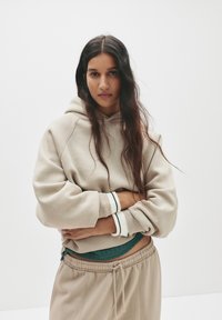 Beige Kapuzenpullover mit lockerer Passform, gerippten Bündchen mit grünen und weißen Streifen, kombiniert mit passenden beigen Jogginghosen.