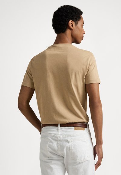 Μπεζ κοντομάνικο μπλουζάκι από μαλακό βαμβάκι, με στρογγυλή λαιμόκοψη. Φορεμένο με λευκό παντελόνι και καφέ ζώνη. Απλός, καθαρός σχεδιασμός.