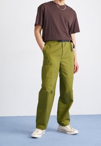 Gröna, lätta cargobyxor med rak passform, prydda med ett svart bälte och sidofickor, kombinerade med en brun t-shirt med kort ärm och vita sneakers.