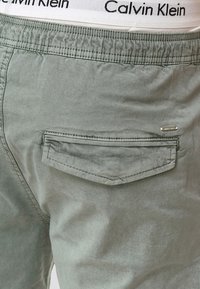 Svijetlozeleni pamučni šorts s elastičnom trakom u struku, s bijelom logotip trakom i stražnjim džepom s diskretnom oznakom branda.