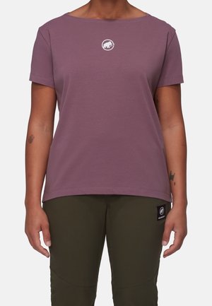 Osoba nosząca krótką bluzkę koloru mauve z białym logo mamuta oraz oliwkowe spodnie z czarną naszywką z logo na udzie.