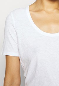 Weißes Baumwoll-T-Shirt mit Rundhalsausschnitt, kurzen Ärmeln und einem weichen, leicht strukturierten Stoff. Ein schlichtes und vielseitiges Design.