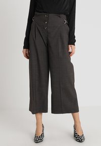 Šedé kostkované kalhoty s širokými nohavicemi a vysokým pasem, s dvojitými knoflíky, kovovými kroužky a čistým zakončením. Vzhledem k černobílým skvrnitým podpatkům.