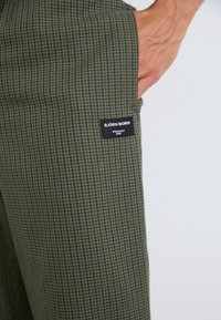 Pantalons à carreaux verts en tissu texturé, avec une étiquette noire sur laquelle est écrit "BJÖRN BORG" en lettres blanches. Coupe slim avec poches latérales.