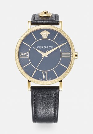 Reloj con correa de cuero negro, caja redonda dorada, dial azul marino, números romanos dorados y un logo de Medusa en la parte superior.