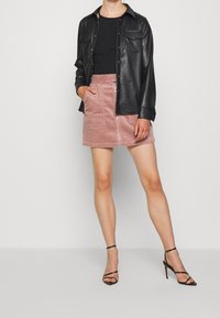 Chemise en cuir noir, haut noir ajusté, jupe mini en velours côtelé rose avec une fermeture éclair à l'avant et des poches, accompagnée de sandales à talons hauts noires à lanières.