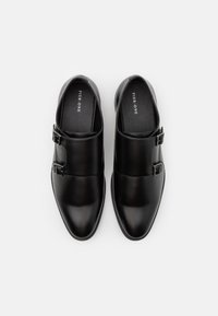 Chaussures en cuir noir avec un nez pointu, présentant des accents de double boucle et une finition lisse ; l'intérieur possède une semelle plate et un revêtement doux.