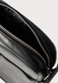 Fekete bőr keresztpántos táska, belsejében steppelt fekete nejlon, ezüst fém cipzárral és elegáns téglalap alakú kialakítással.