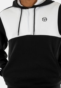 Felpa con zip bianca e nera con una grande striscia nera sul petto, dotata di un logo sul lato sinistro e cappuccio con cordino regolabile.