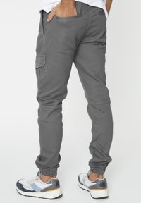 Grijze jogger-stijl broek met elastische boorden, voorzien van zijzakken en een relaxte pasvorm. Gecombineerd met meerkleurige sportschoenen.